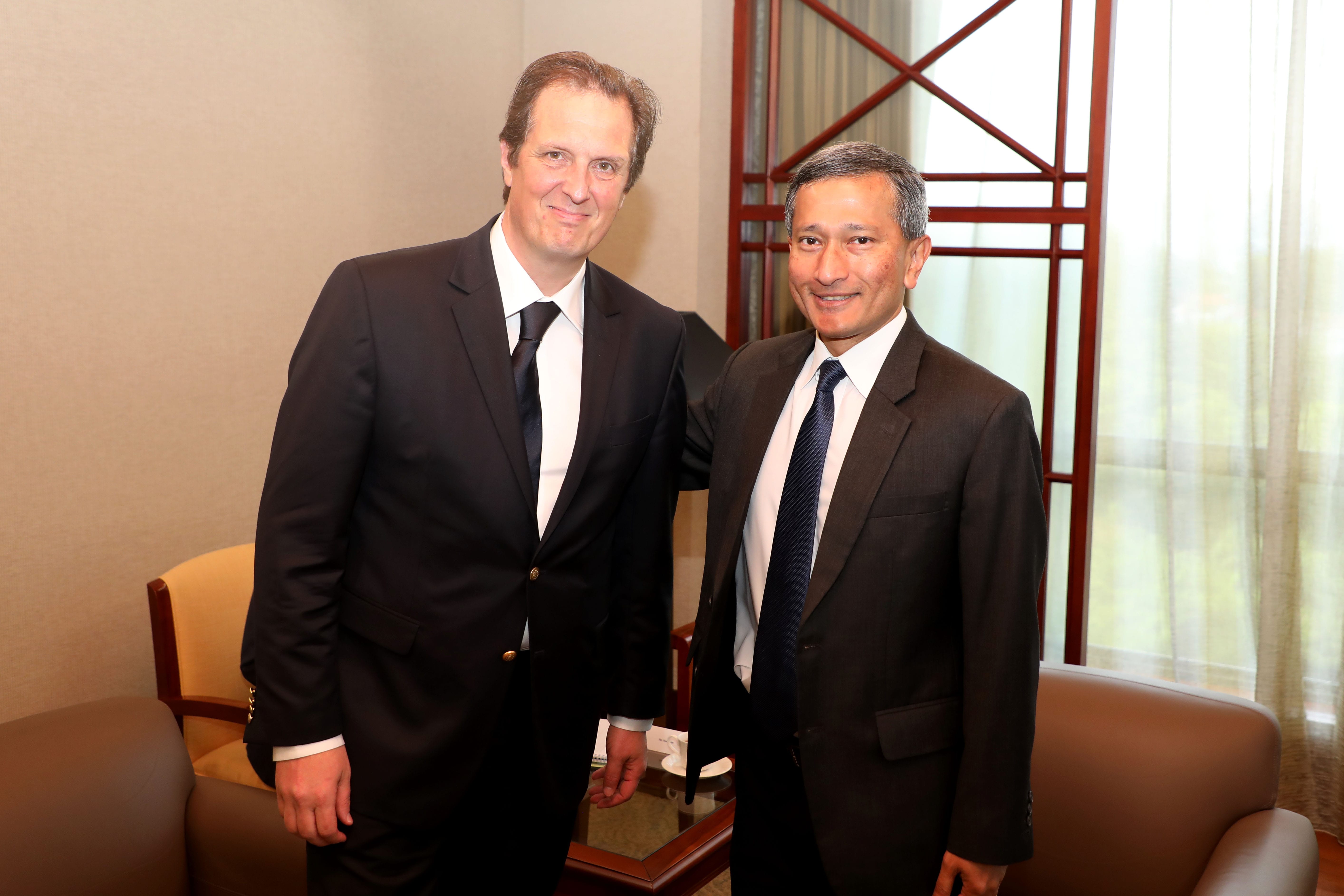Two men in suits pose indoors with arms around each other.